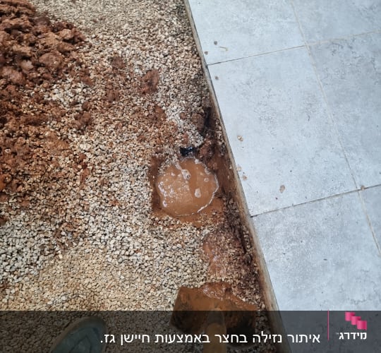 חפירה באדמה עם מים דולפים ליד שביל מרוצף